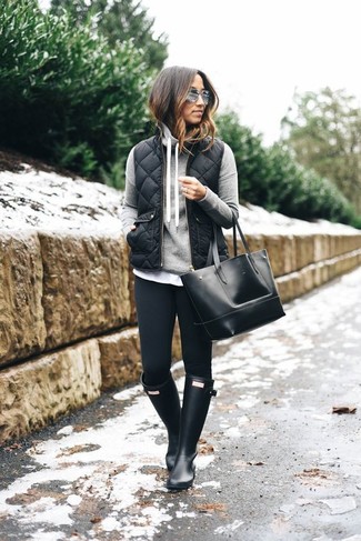 schwarze ärmellose Jacke, grauer Pullover mit einer Kapuze, schwarze Leggings, schwarze Gummistiefel für Damen
