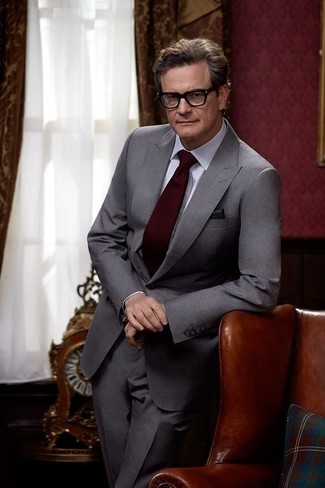 Colin Firth trägt grauer Anzug, weißes Businesshemd, dunkelrote Krawatte, schwarzes Einstecktuch