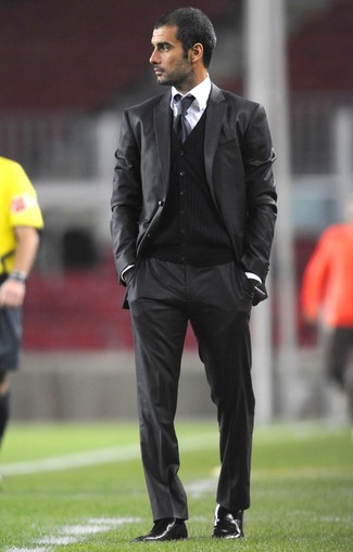 Pep Guardiola trägt dunkelgrauer Anzug, schwarze Strickjacke, weißes Businesshemd, schwarze Chelsea-Stiefel aus Leder
