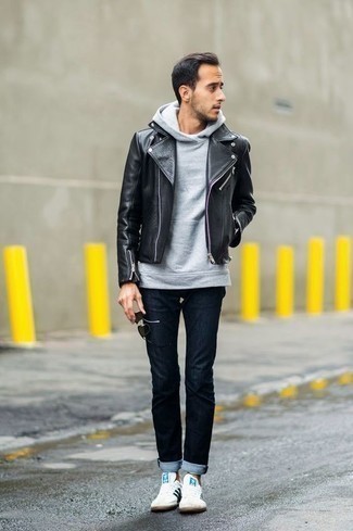 schwarze Leder Bikerjacke, grauer Pullover mit einem Kapuze, dunkelblaue Jeans, weiße und schwarze Segeltuch niedrige Sneakers für Herren