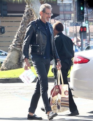 Jeff Goldblum trägt schwarze Leder Bikerjacke, dunkelblaues Polohemd, dunkelgraue Chinohose, schwarze und weiße Leder Slipper