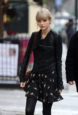 Taylor Swift trägt schwarze Wildleder Bikerjacke, schwarzes bedrucktes Skaterkleid, dunkelbraune Leder Umhängetasche, schwarze Strumpfhose