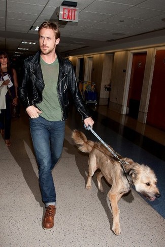 Ryan Gosling trägt schwarze Leder Bikerjacke, olivgrünes T-Shirt mit einem Rundhalsausschnitt, dunkelblaue Jeans, braune Lederarbeitsstiefel