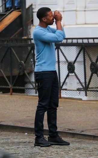 Michael B. Jordan trägt blauer Pullover mit einem Rundhalsausschnitt, schwarze Jeans, dunkelbraune Sportschuhe