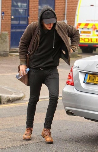 Harry Styles trägt braune Bomberjacke, schwarzer Pullover mit einem Kapuze, schwarze enge Jeans, beige Lederfreizeitstiefel