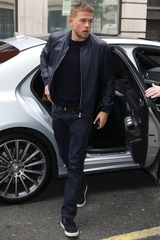 Charlie Hunnam trägt dunkelblaue Leder Bomberjacke, schwarzer Pullover mit einem Rundhalsausschnitt, dunkelblaue Jeans, schwarze niedrige Sneakers