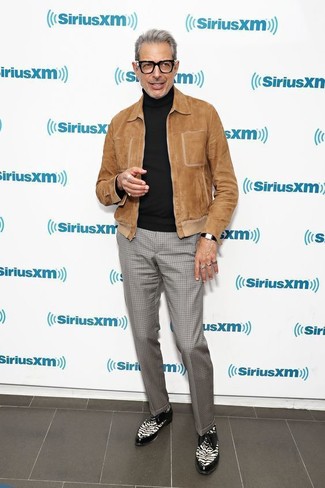 Jeff Goldblum trägt braune Wildleder Bomberjacke, schwarzer Rollkragenpullover, graue Anzughose mit Karomuster, schwarze und weiße Leder Derby Schuhe
