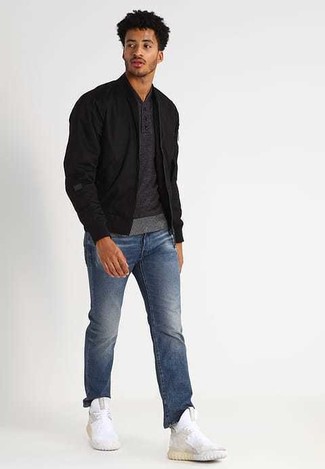schwarze Bomberjacke, dunkelgrauer Henley-Pullover, blaue Jeans, weiße Sportschuhe für Herren