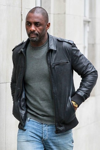 Idris Elba trägt schwarze Leder Bomberjacke, dunkelgrüner Pullover mit einem Rundhalsausschnitt, hellblaue Jeans, goldene Uhr