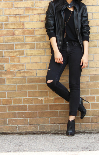 schwarze Leder Bomberjacke, schwarzes T-Shirt mit einem Rundhalsausschnitt, schwarze enge Jeans mit Destroyed-Effekten, schwarze Leder Stiefeletten für Damen