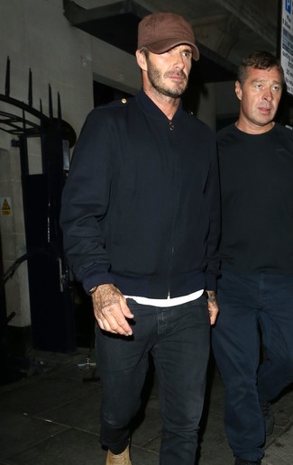 David Beckham trägt dunkelblaue Bomberjacke, weißes T-Shirt mit einem Rundhalsausschnitt, schwarze Jeans, beige Wildlederfreizeitstiefel