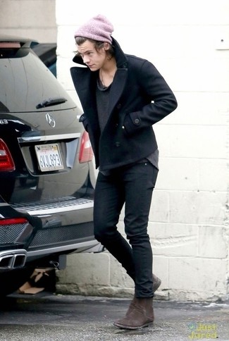 Harry Styles trägt schwarze Cabanjacke, dunkelgrauer Pullover mit einem Rundhalsausschnitt, schwarze enge Jeans, dunkelbraune Chelsea-Stiefel aus Wildleder