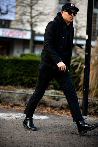 schwarze Collegejacke, schwarzer Pullover mit einem Kapuze, schwarze Jeans, schwarze Lederformelle stiefel für Herren