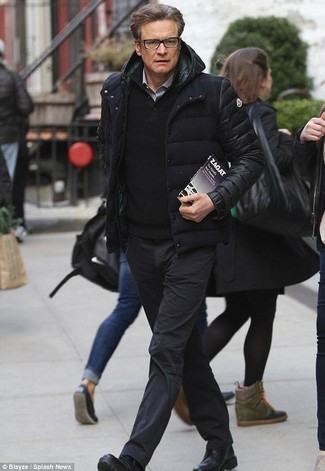 Colin Firth trägt schwarze Daunenjacke, schwarzer Pullover mit einem zugeknöpften Kragen, graues Langarmhemd, schwarze Chinohose