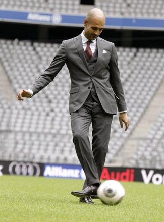 Pep Guardiola trägt grauer Dreiteiler, weißes Businesshemd, dunkelrote Leder Oxford Schuhe, dunkelrote bedruckte Krawatte