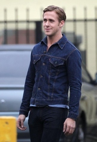 Ryan Gosling trägt dunkelblaue Jeansjacke, hellblaues T-Shirt mit einem Rundhalsausschnitt, schwarze Jeans