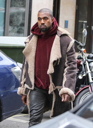 Kanye West trägt dunkelbraune Lammfelljacke, dunkelroter Samtpullover mit einem kapuze, schwarze Lederjeans