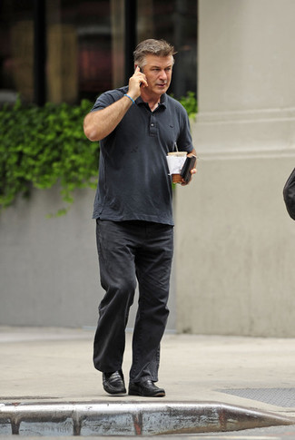 Alec Baldwin trägt dunkelgraues Polohemd, schwarze Jeans, schwarze Leder Slipper