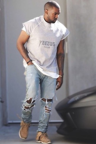 Kanye West trägt graues bedrucktes T-Shirt mit einem Rundhalsausschnitt, hellblaue Jeans mit Destroyed-Effekten, beige Sportschuhe