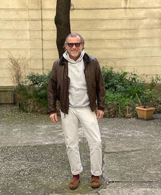 dunkelbraune Harrington-Jacke aus Leder, grauer Pullover mit einem Kapuze, weiße Jeans, braune Wildleder Slipper mit Quasten für Herren
