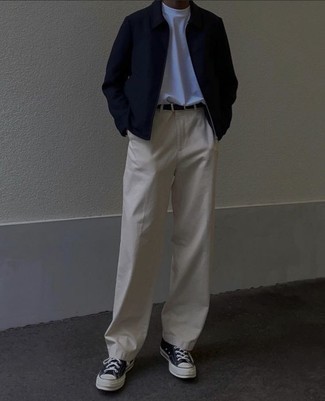 schwarze Harrington-Jacke, weißes T-Shirt mit einem Rundhalsausschnitt, hellbeige Chinohose, schwarze und weiße Segeltuch niedrige Sneakers für Herren