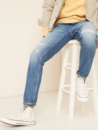 hellbeige Jeansjacke, gelber Pullover mit einem Kapuze, blaue Jeans mit Destroyed-Effekten, weiße hohe Sneakers aus Segeltuch für Herren