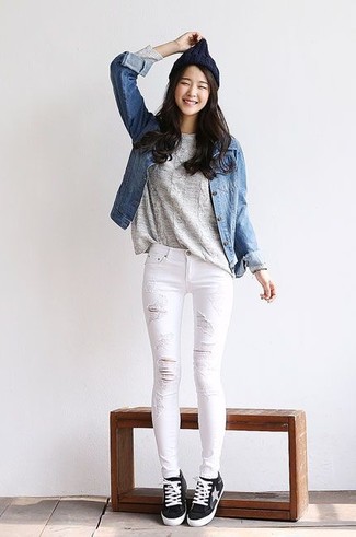 blaue Jeansjacke, grauer Strickpullover, weiße enge Jeans mit Destroyed-Effekten, schwarze und weiße niedrige Sneakers für Damen