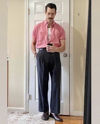 Sommer Outfits Herren 2024: Tragen Sie ein rosa Kurzarmhemd und eine dunkelblaue Anzughose, um vor Klasse und Perfektion zu strotzen. Fühlen Sie sich ideenreich? Vervollständigen Sie Ihr Outfit mit dunkelbraunen Leder Slippern. So ist der Look total sommertauglich.