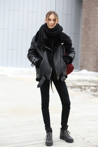schwarze Lammfelljacke, schwarzer Oversize Pullover, schwarze enge Jeans, schwarze flache Stiefel mit einer Schnürung aus Leder für Damen