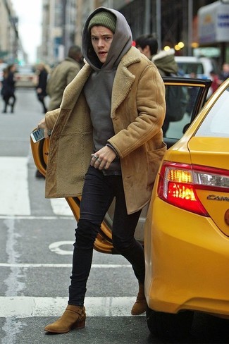 Harry Styles trägt beige Lammfellmantel, grauer Pullover mit einem Kapuze, schwarze enge Jeans, beige Chelsea-Stiefel aus Wildleder