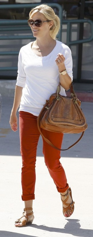 Reese Witherspoon trägt weißes Langarmshirt, rote Chinohose, braune Römersandalen aus Leder, braune Satchel-Tasche aus Leder
