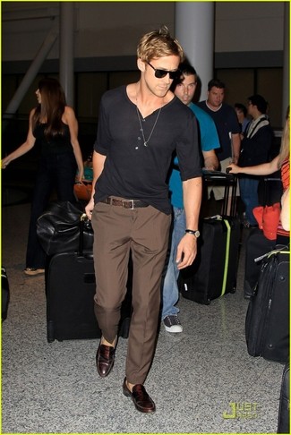 Ryan Gosling trägt schwarzes Langarmshirt mit einer Knopfleiste, braune Anzughose, dunkelbraune Leder Slipper, brauner Ledergürtel