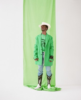 Lil Nas X trägt grüner Mantel, grünes bedrucktes Sweatshirt, hellblaue Jeans, schwarze und weiße Cowboystiefel aus Leder