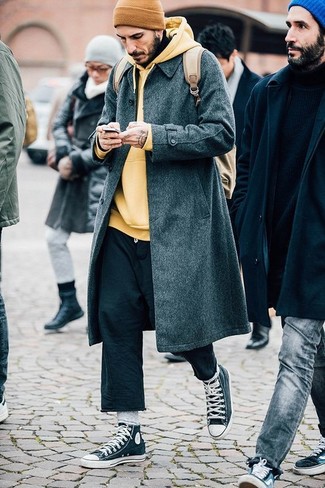 dunkelgrauer Mantel, gelber Pullover mit einem Kapuze, schwarze Chinohose, dunkelgraue hohe Sneakers für Herren