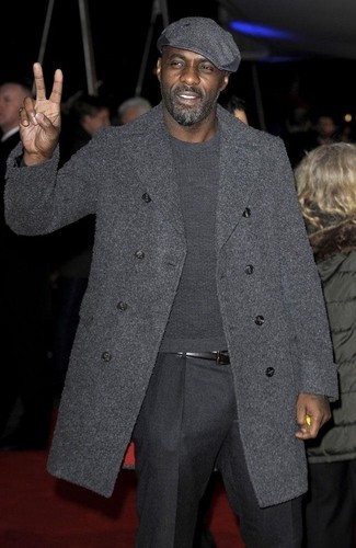 Idris Elba trägt dunkelgrauer Mantel, dunkelgrauer Pullover mit einem Rundhalsausschnitt, dunkelgraue Wollanzughose, dunkelgraue Schiebermütze