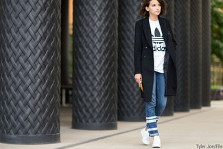 schwarzer Mantel, weißes und schwarzes bedrucktes T-Shirt mit einem Rundhalsausschnitt, blaue horizontal gestreifte Jeans, weiße niedrige Sneakers für Damen