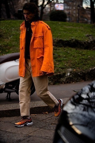 orange Militärjacke, schwarzer Pullover mit einem Kapuze, beige Chinohose, orange Sportschuhe für Herren
