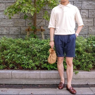 Smart-Casual heiß Wetter Outfits Herren 2024: Kombinieren Sie ein weißes Polohemd mit dunkelblauen Shorts für ein Alltagsoutfit, das Charakter und Persönlichkeit ausstrahlt. Setzen Sie bei den Schuhen auf die klassische Variante mit braunen Leder Slippern mit Quasten.