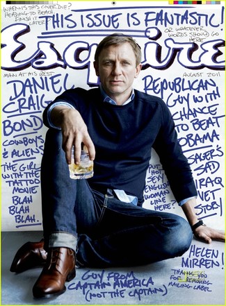 Daniel Craig trägt dunkelblauer Pullover mit einem Rundhalsausschnitt, blaues Businesshemd, dunkelblaue Jeans, braune Leder Derby Schuhe