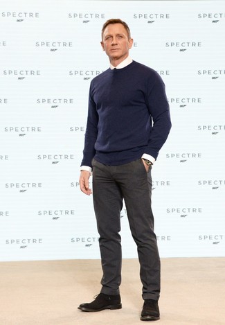 Daniel Craig trägt dunkelblauer Pullover mit einem Rundhalsausschnitt, weißes Businesshemd, dunkelbraune Wollanzughose, dunkelbraune Chukka-Stiefel aus Wildleder