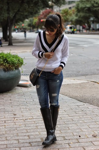 weißer und schwarzer Pullover mit einem V-Ausschnitt, dunkelblaue enge Jeans mit Destroyed-Effekten, schwarze kniehohe Stiefel aus Leder, schwarze Leder Umhängetasche für Damen