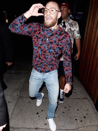 Conor McGregor trägt roter Camouflage Pullover mit einem Rundhalsausschnitt, hellblaue Jeans, weiße niedrige Sneakers