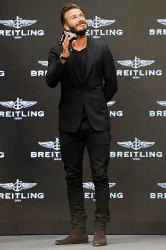 David Beckham trägt schwarzes Sakko, schwarzes T-Shirt mit einem Rundhalsausschnitt, schwarze Jeans, dunkelbraune Chelsea-Stiefel aus Wildleder