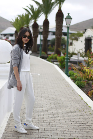 graue Strick Strickjacke mit einer offenen Front, weißer Jumpsuit, weiße niedrige Sneakers, schwarze Sonnenbrille für Damen