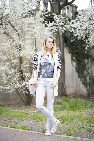 hellbeige Strickjacke mit einer offenen Front mit geometrischen Mustern, weißes und schwarzes bedrucktes T-Shirt mit einem Rundhalsausschnitt, weiße enge Jeans, weiße hohe Sneakers aus Segeltuch für Damen