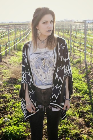 schwarze und weiße Strickjacke mit einer offenen Front mit geometrischen Mustern, graues bedrucktes T-Shirt mit einem Rundhalsausschnitt, dunkelgraue Jeansshorts, silberner Anhänger für Damen