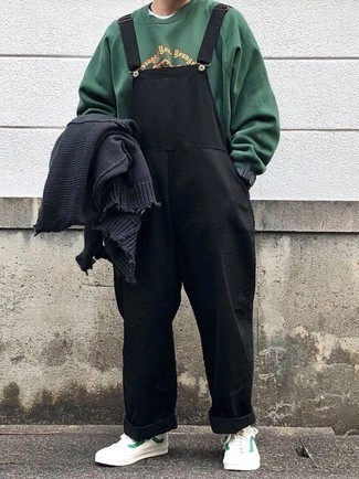 dunkelgraue Strickjacke, dunkelgrünes bedrucktes Sweatshirt, schwarze Latzhose, weiße und grüne Segeltuch niedrige Sneakers für Herren