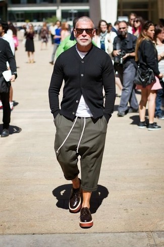 Nick Wooster trägt schwarze Strickjacke, weißes T-Shirt mit einem Rundhalsausschnitt, olivgrüne Jogginghose, dunkelbraune Leder Derby Schuhe