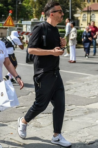 schwarzes T-Shirt mit einem Rundhalsausschnitt, schwarze Chinohose, weiße und schwarze Leder niedrige Sneakers, schwarzer Leder Rucksack für Herren