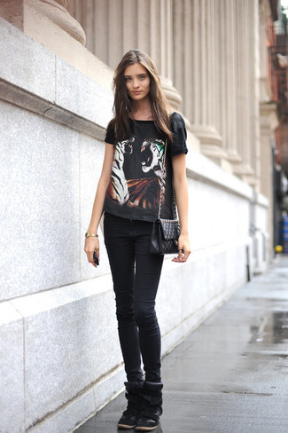 schwarzes bedrucktes T-Shirt mit einem Rundhalsausschnitt, schwarze enge Jeans, schwarze Wildleder Keil Turnschuhe, schwarze gesteppte Leder Umhängetasche für Damen